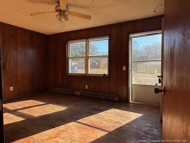 unfurnished room featuring ceiling fan, a textured ceiling, wooden walls, and a baseboard heating unit