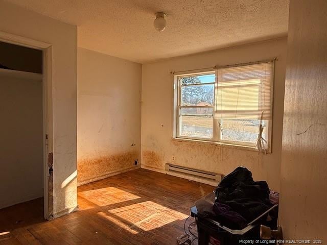 unfurnished bedroom featuring wood-type flooring, a textured ceiling, and a baseboard heating unit