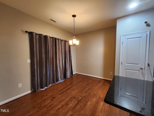 spare room featuring a chandelier and dark wood-type flooring