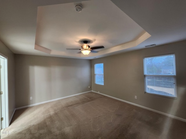 carpeted spare room featuring a tray ceiling, a wealth of natural light, and ceiling fan