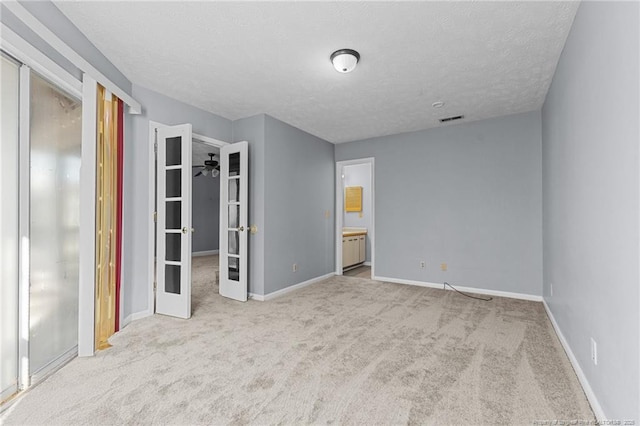 unfurnished bedroom with a textured ceiling, ensuite bathroom, light carpet, and french doors