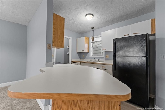 kitchen featuring black fridge, a textured ceiling, sink, white cabinetry, and hanging light fixtures