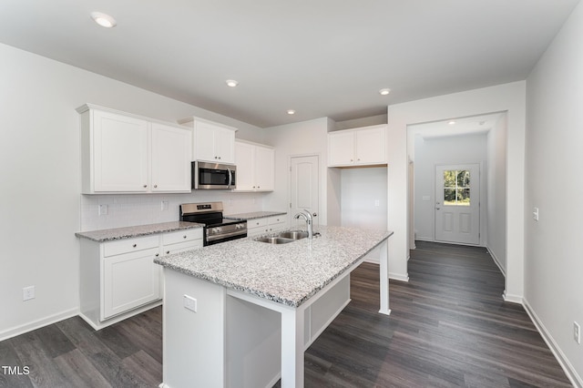 kitchen with light stone counters, stainless steel appliances, sink, white cabinets, and an island with sink