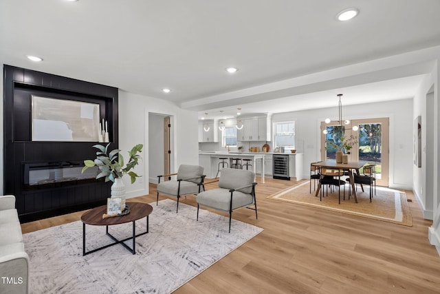 living room with a large fireplace, light wood-type flooring, wine cooler, and an inviting chandelier