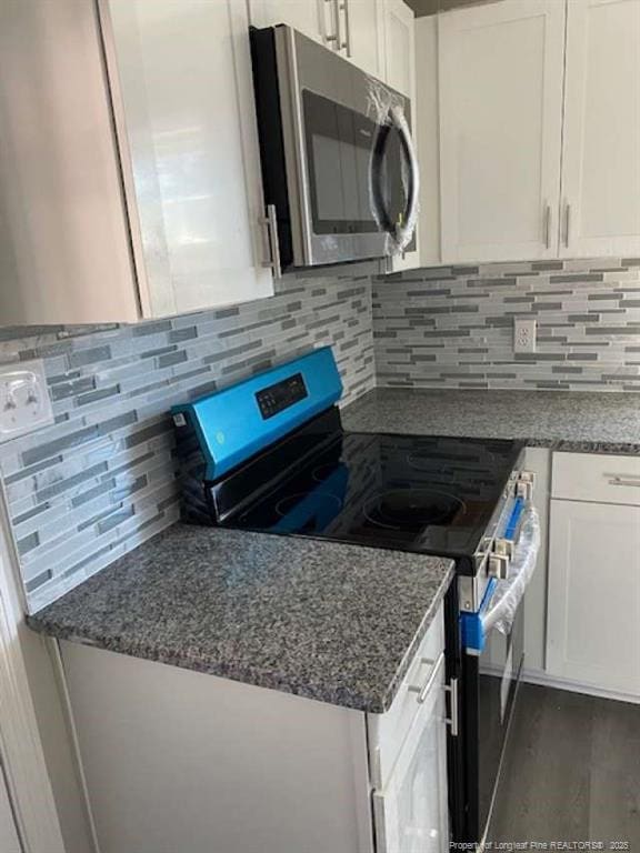 kitchen featuring white cabinetry, dark wood-type flooring, stainless steel appliances, dark stone countertops, and decorative backsplash