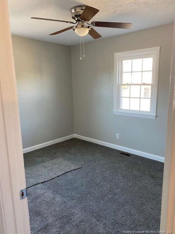 empty room featuring ceiling fan, a textured ceiling, and dark colored carpet