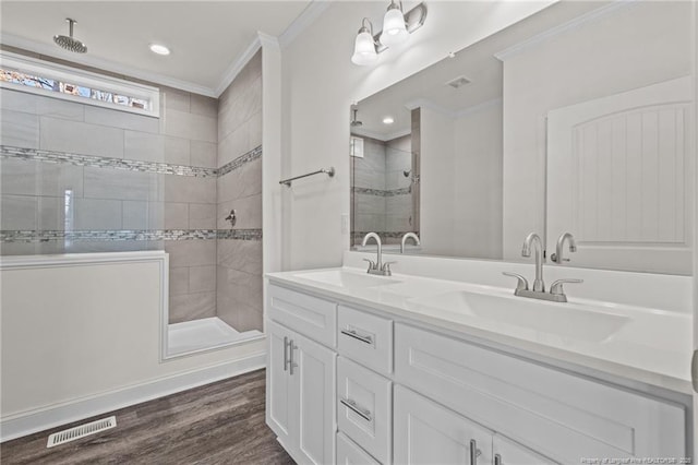 bathroom featuring a tile shower, hardwood / wood-style floors, vanity, and ornamental molding