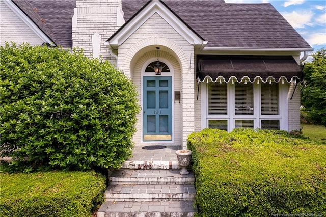 view of exterior entry with roof with shingles and brick siding