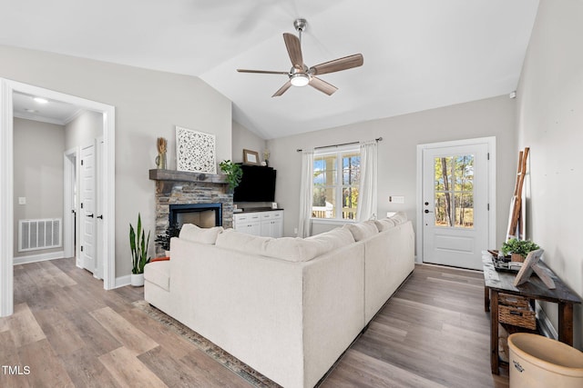 living room featuring a stone fireplace, ceiling fan, vaulted ceiling, and light wood-type flooring