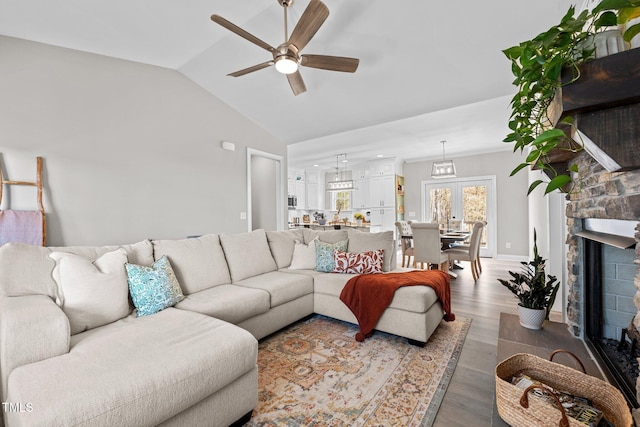 living room featuring ceiling fan, hardwood / wood-style floors, vaulted ceiling, and a brick fireplace