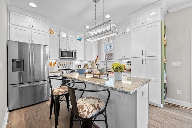 kitchen with a center island, hanging light fixtures, appliances with stainless steel finishes, light stone counters, and white cabinetry