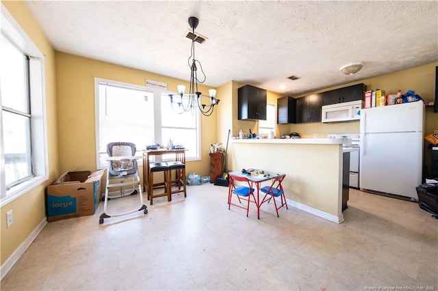 kitchen featuring hanging light fixtures, a notable chandelier, kitchen peninsula, a textured ceiling, and white appliances