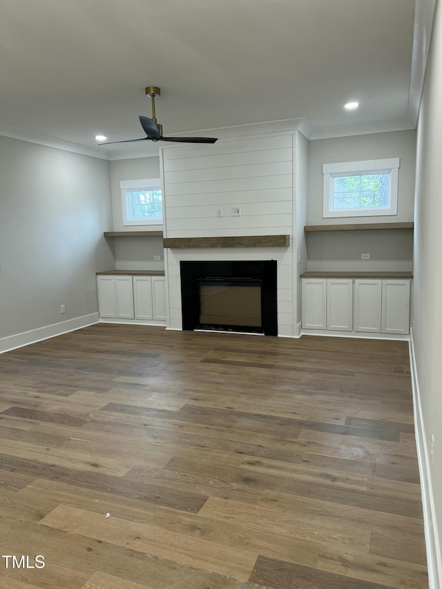 unfurnished living room featuring a fireplace, wood-type flooring, ceiling fan, and crown molding