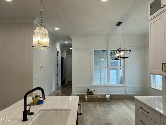 kitchen with sink, hanging light fixtures, ornamental molding, light stone counters, and white cabinetry