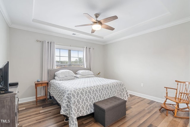 bedroom featuring crown molding, dark hardwood / wood-style floors, ceiling fan, and a tray ceiling