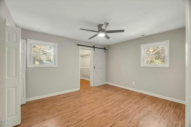 unfurnished bedroom with ceiling fan, a barn door, a spacious closet, light hardwood / wood-style floors, and a closet