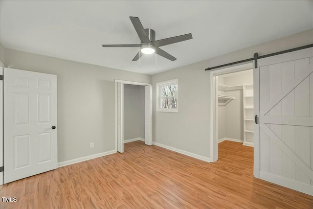 unfurnished bedroom featuring light wood-type flooring, ceiling fan, a barn door, a spacious closet, and a closet