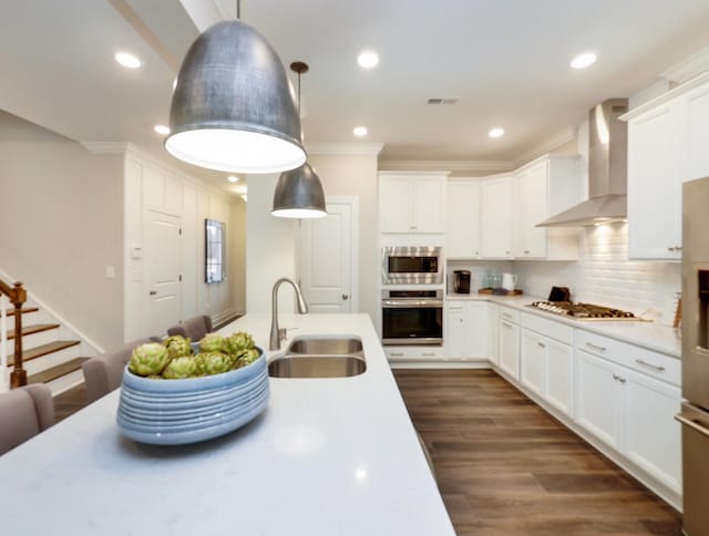 kitchen featuring sink, hanging light fixtures, stainless steel appliances, wall chimney range hood, and white cabinets