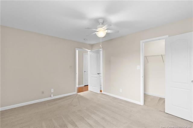 unfurnished bedroom with ceiling fan, a closet, a spacious closet, and light carpet