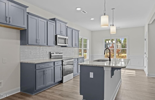 kitchen featuring gray cabinetry, stainless steel appliances, sink, pendant lighting, and an island with sink