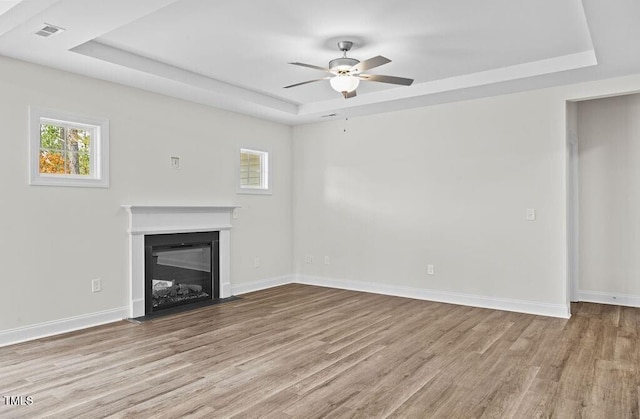 unfurnished living room featuring light wood-type flooring, a raised ceiling, and ceiling fan