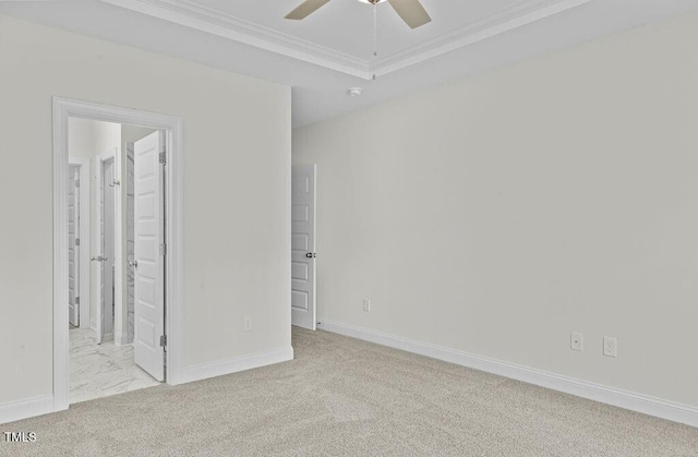 unfurnished bedroom featuring a raised ceiling, crown molding, ensuite bath, ceiling fan, and light colored carpet