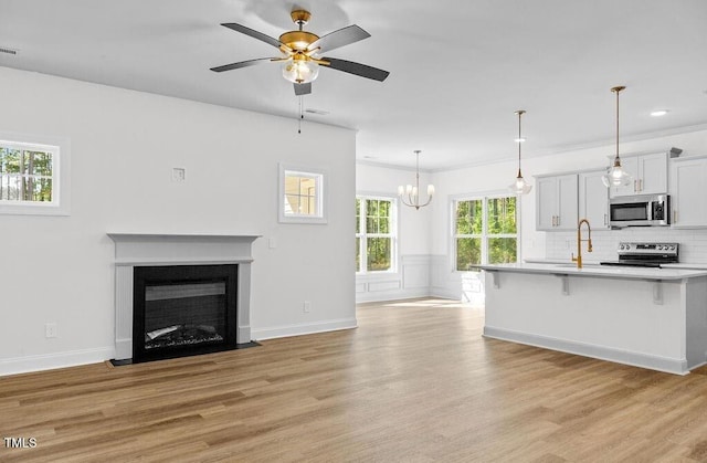 unfurnished living room featuring sink, light hardwood / wood-style floors, ceiling fan with notable chandelier, and ornamental molding