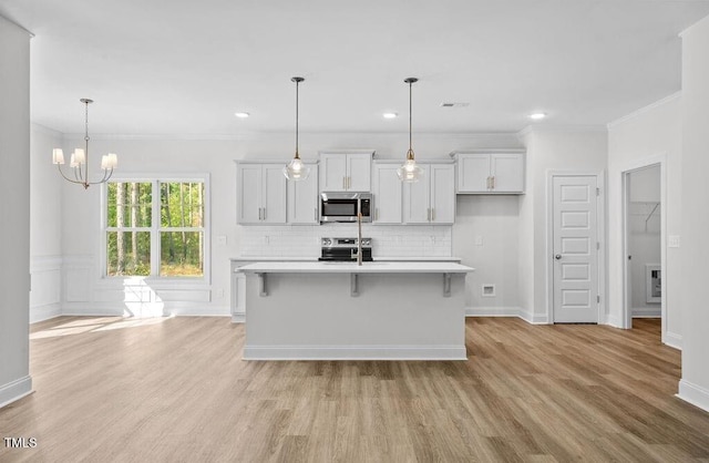 kitchen featuring appliances with stainless steel finishes, a breakfast bar, crown molding, a center island with sink, and hanging light fixtures