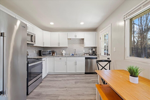 kitchen with decorative backsplash, appliances with stainless steel finishes, light stone counters, sink, and white cabinetry