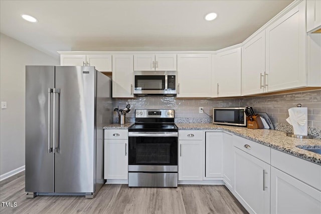 kitchen featuring appliances with stainless steel finishes, light wood-type flooring, white cabinetry, and light stone counters