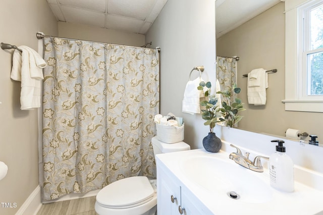 bathroom with a drop ceiling, vanity, a healthy amount of sunlight, and toilet