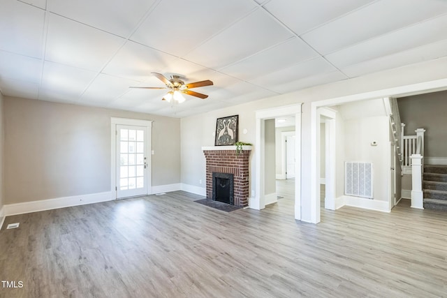 unfurnished living room featuring a paneled ceiling, ceiling fan, light wood-type flooring, and a brick fireplace