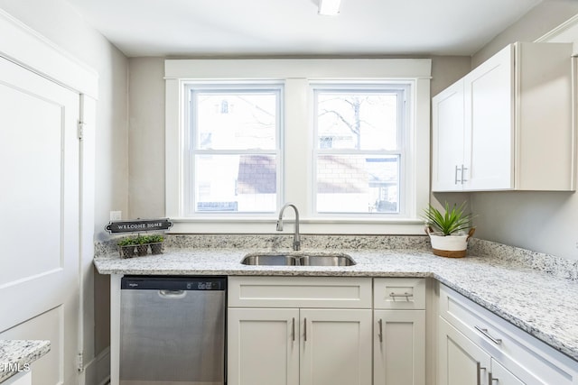 kitchen featuring light stone counters, white cabinetry, stainless steel dishwasher, and sink