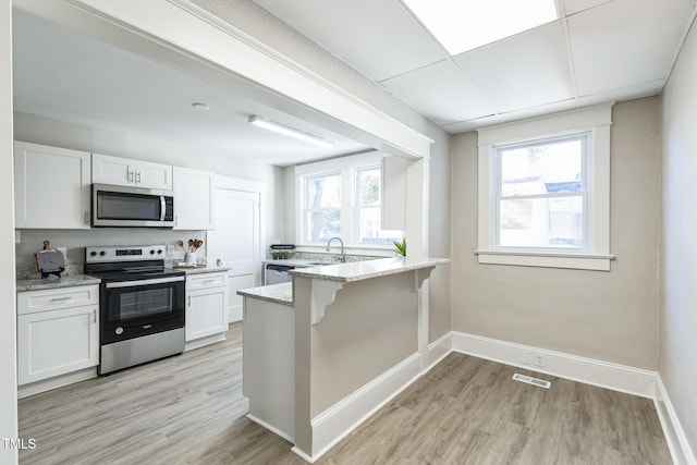 kitchen with a wealth of natural light, white cabinetry, light stone countertops, and appliances with stainless steel finishes