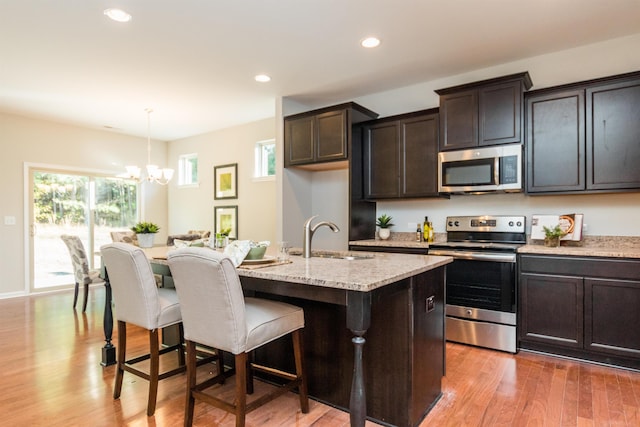 kitchen with pendant lighting, a center island with sink, sink, appliances with stainless steel finishes, and a notable chandelier