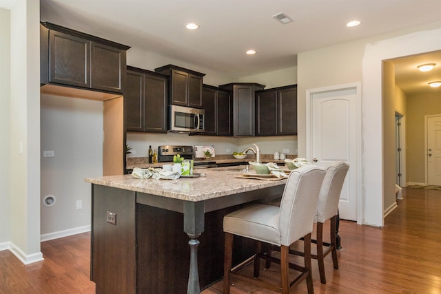 kitchen with dark hardwood / wood-style floors, sink, stainless steel appliances, and an island with sink