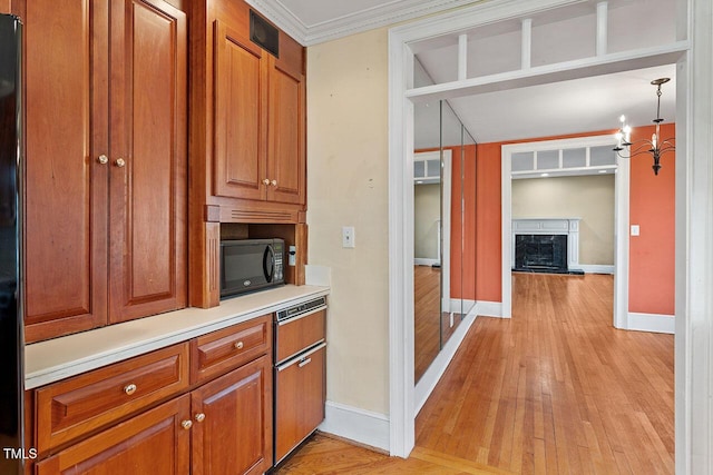 kitchen with crown molding, an inviting chandelier, light wood-type flooring, pendant lighting, and a high end fireplace