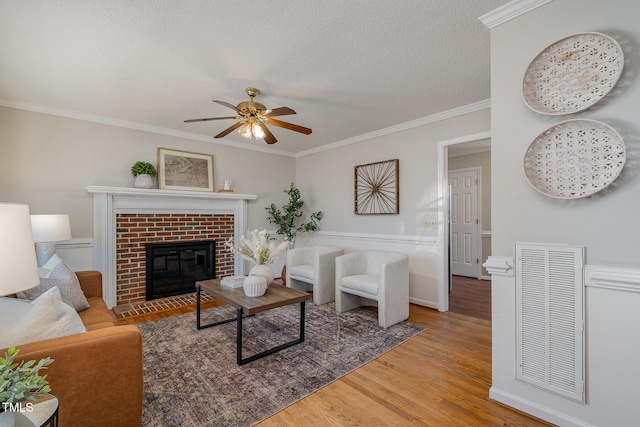 living room with a fireplace, a textured ceiling, ceiling fan, ornamental molding, and hardwood / wood-style flooring