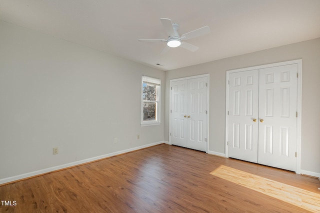 unfurnished bedroom with ceiling fan, hardwood / wood-style floors, and two closets