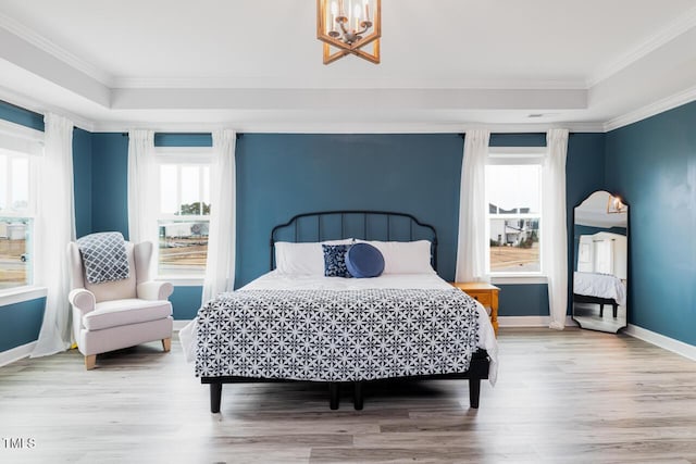 bedroom with an inviting chandelier, wood-type flooring, ornamental molding, and a tray ceiling