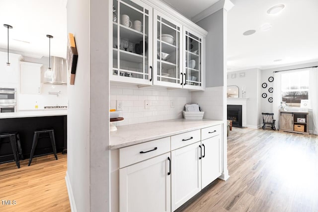 kitchen featuring light hardwood / wood-style flooring, backsplash, decorative light fixtures, white cabinets, and ornamental molding