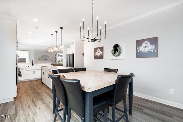 dining space with sink, ornamental molding, a notable chandelier, and hardwood / wood-style flooring