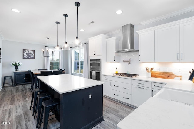 kitchen with wall chimney exhaust hood, tasteful backsplash, decorative light fixtures, white cabinets, and appliances with stainless steel finishes