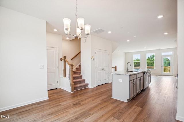 kitchen featuring sink, decorative light fixtures, stainless steel dishwasher, a notable chandelier, and a kitchen island with sink