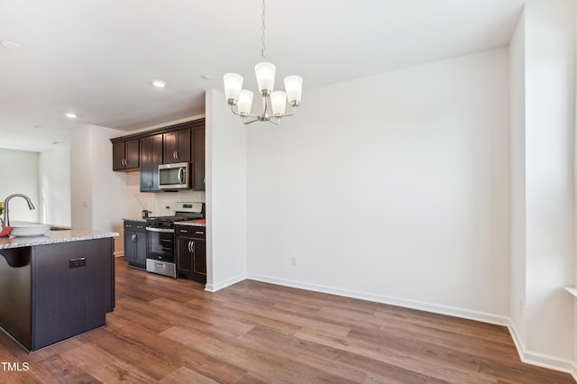 kitchen with dark brown cabinetry, stainless steel appliances, an inviting chandelier, pendant lighting, and hardwood / wood-style flooring