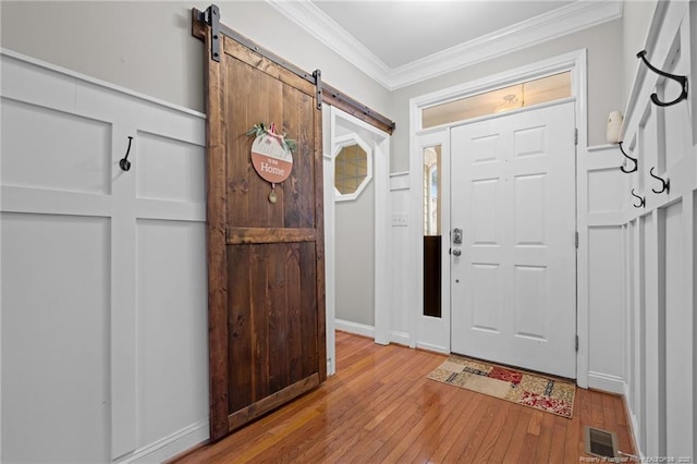 entryway with visible vents, light wood-style flooring, crown molding, and a barn door