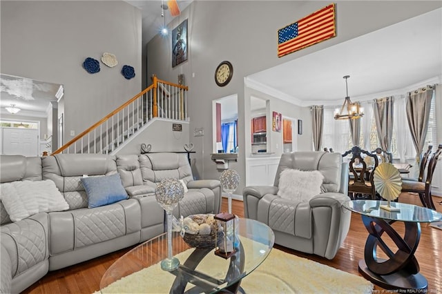 living room featuring wood finished floors, stairway, a high ceiling, crown molding, and a chandelier