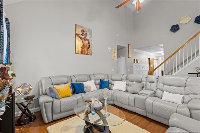 living room featuring a ceiling fan, stairs, a towering ceiling, and wood finished floors