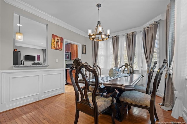 dining area with an inviting chandelier, crown molding, and light wood-style floors