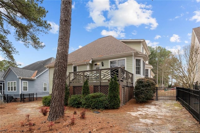 rear view of house with a shingled roof, a deck, and fence